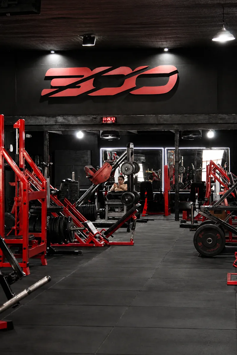 Máquinas de musculación rojas bajo el logo de 300 en la sala